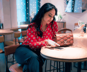 leila sitting at a table pointing at her phone