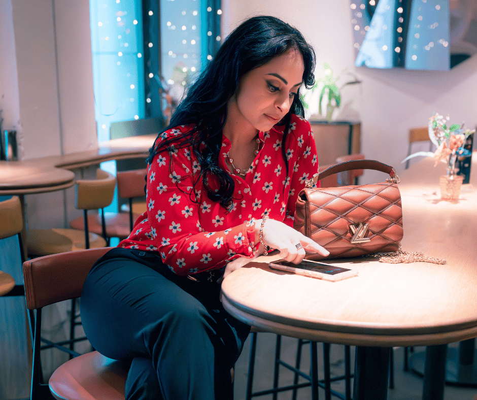 leila sitting at a table pointing at her phone